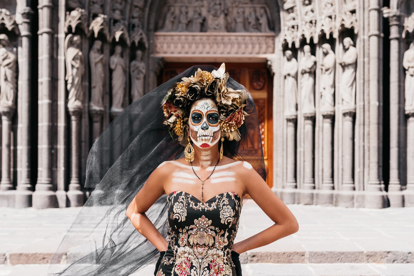 une femme avec une coiffe de fleur , le visage maquiller en tete de mort avec une robe bustier devant une cathedrale